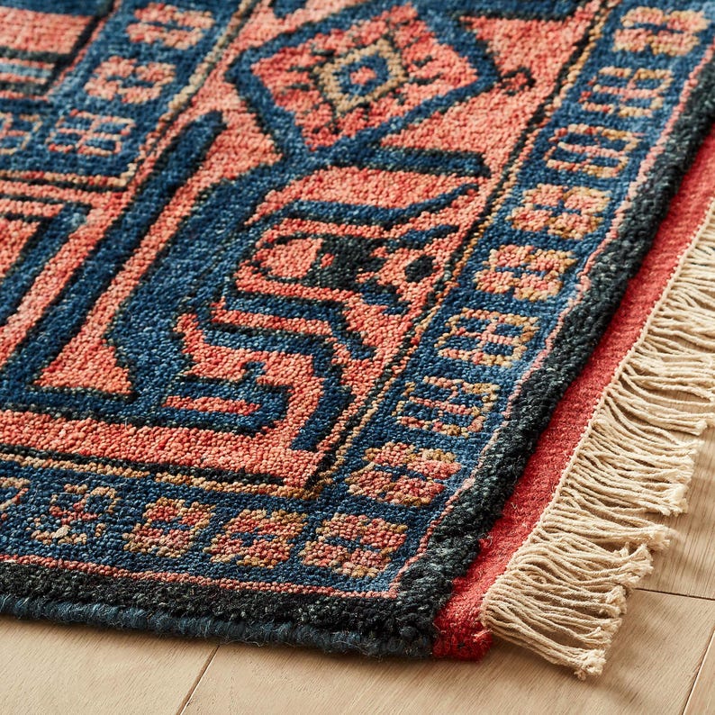 Close-up of a patterned oushak rug with blue and red colors on a wooden floor.