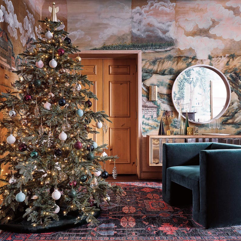 Decorated Christmas tree in a living room with a green sofa, patterned wall and hand knotted oushak rug from Bisha Rugs.