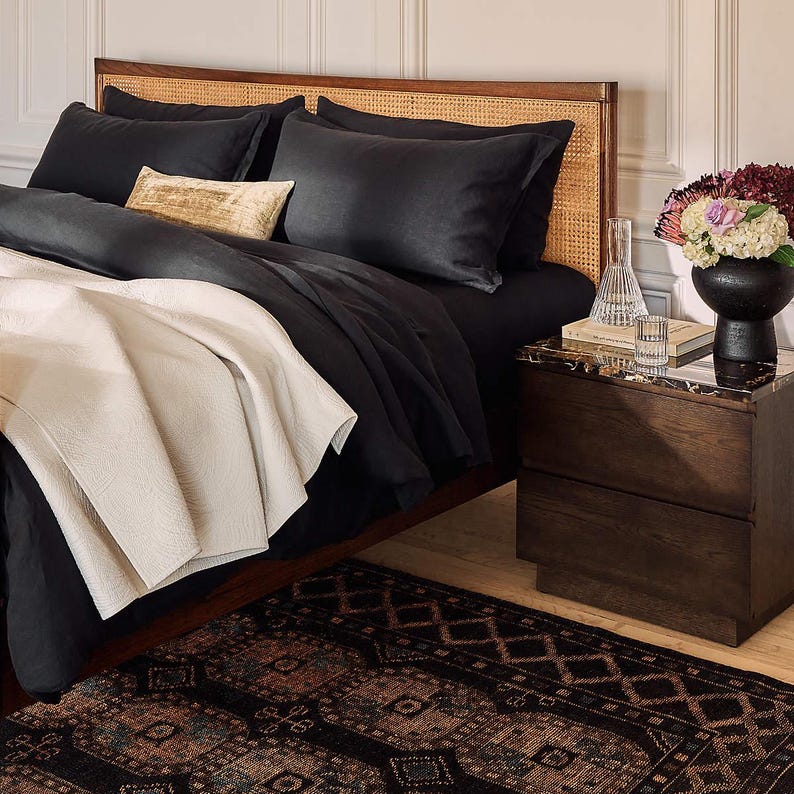 Bedroom with black bedding, wooden headboard, and nightstand with decorative items and Hand knotted Oushak Rug.